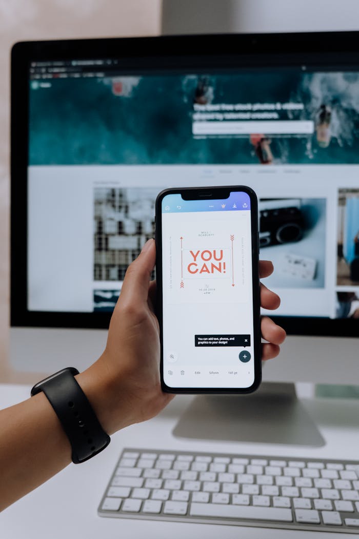 Hand holding smartphone with You Can! message in front of desktop screen.